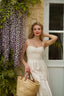 A blonde surrounded by enchanting flowers in scenic Normandy, wearing a cream colored corset dress.