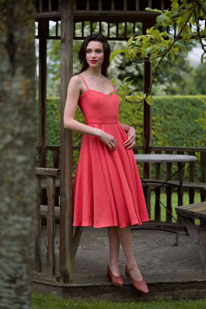 A brunette girl standing against the backdrop of a castle in France, wearing a Brigitte Bardot inspired red linen dress as a guest to a wedding. 