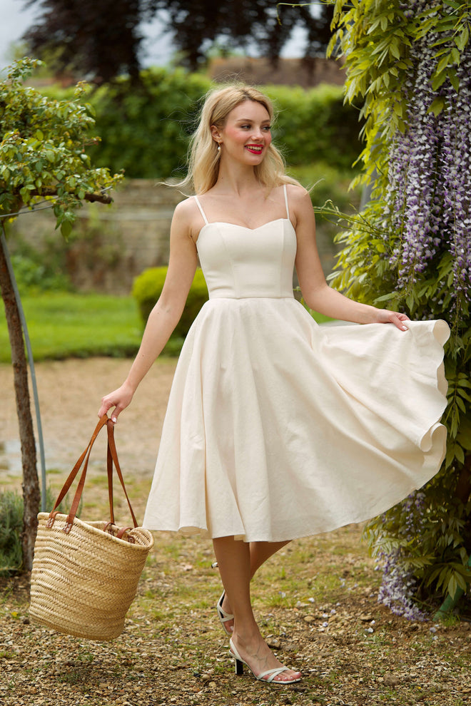 A beautiful girl surrounded by enchanting flowers in scenic Normandy, wearing a cream colored corset dress.