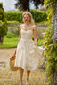 A beautiful blonde girl surrounded by enchanting flowers in scenic Normandy, wearing a cream colored corset dress.