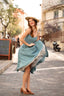 A laughing redhead in Cannes wearing a sunhat and a blue cotton/linen Gaâla Bardot dress, lifting up the skirt to show a voluminous petticoat underneath.