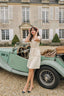 A girl in France, leaning against a vintage car and wearing Gaâla Paris belted button down Paris dress