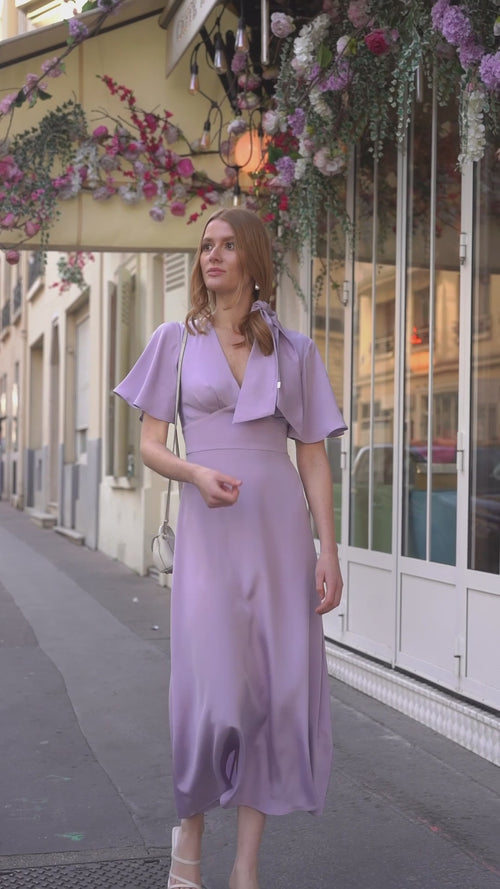A girl in front of a cafe in Paris wearing a long silk lilac colored dress