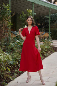 A smiling girl in a long red silk Gaâla dress moving playfully around in Paris. 