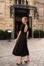 A girl standing in front of a fancy hotel in Paris wearing a long black evening dress from Gaâla