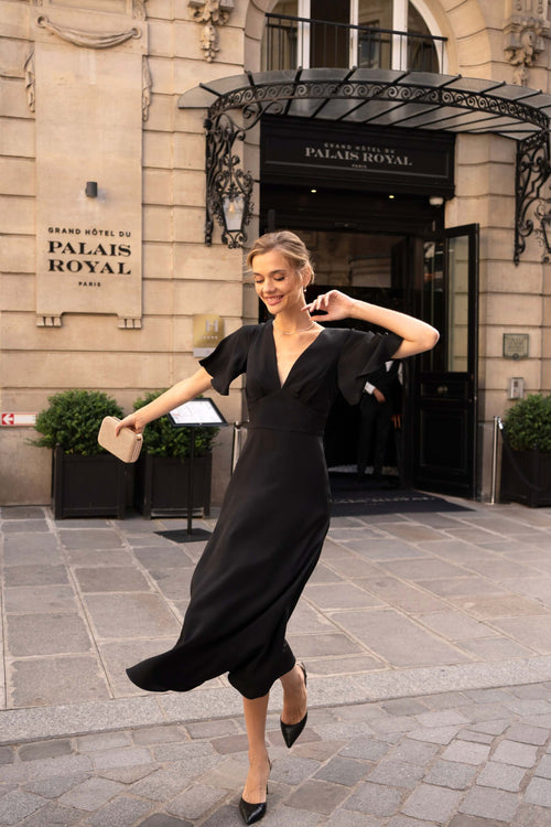 A girl standing in front of a hotel in Paris wearing a long black evening dress from Gaâla