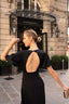 A blonde girl standing in front of a fancy hotel in Paris wearing a long black evening dress from Gaâla