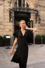 A blonde girl standing in front of a hotel in Paris wearing a long black evening dress from Gaâla