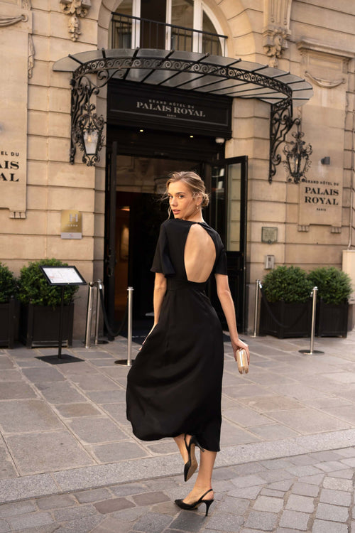 A blonde standing in front of a fancy hotel in Paris wearing a long black evening dress from Gaâla