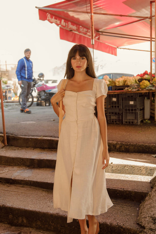 Brunette girl in a marketplace in Sicily, wearing a vintage inspired button down cream Gaâla dress