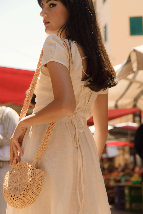 Brunette in a marketplace in Sicily, wearing a vintage inspired button down cream Gaâla linen dress