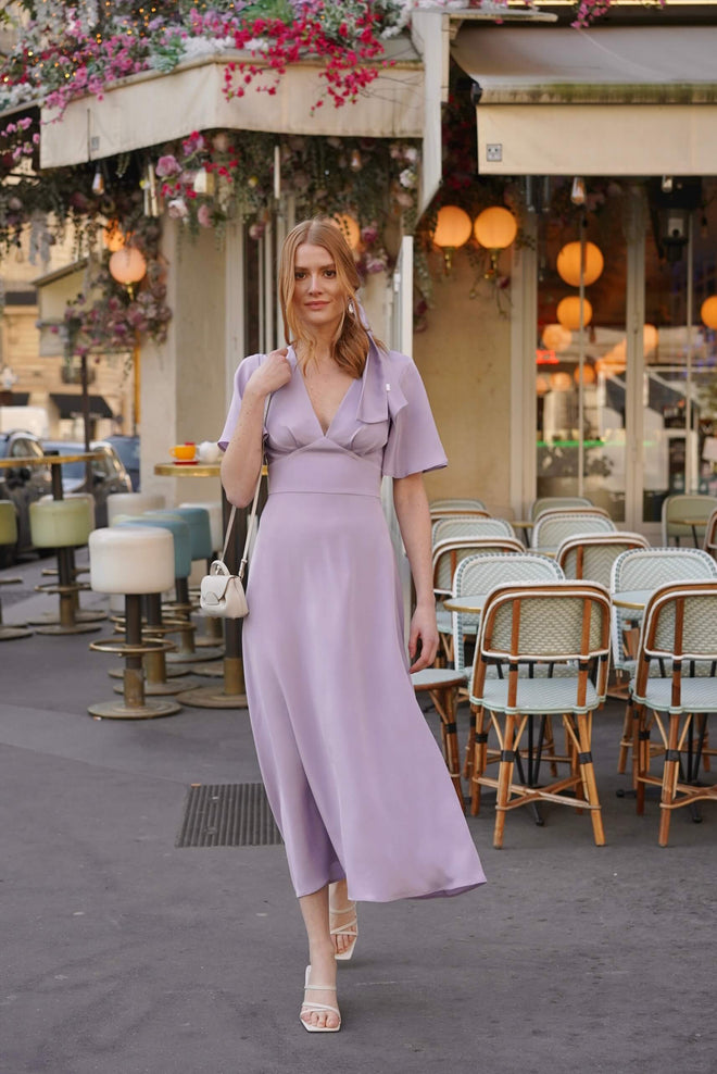 A redhead girl in front of a cafe in Paris wearing a long silk lilac colored dress