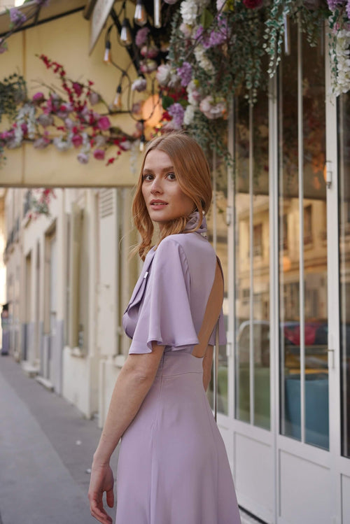A girl in front of a cafe in Paris wearing a long silk lilac dress
