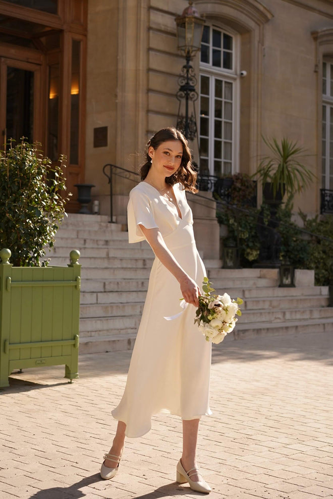 A bride on her wedding day in Paris wearing a long silk dress with flutter sleeves and an open back from Gaâla