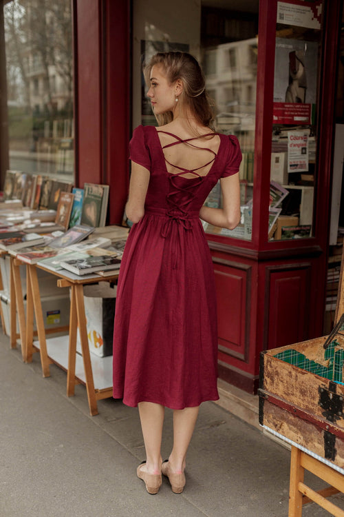 A blonde girl in Paris at a vintage book shop wearing a bordeaux button down Gaâla dress
