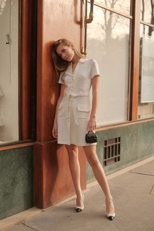A blonde girl in Paris leaning against a wall wearing a white belted Gaâla dress
