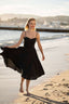 A blonde girl recreating Brigitte Bardot’s run on the beach in Cannes, wearing a Gaâla cotton/linen black Bardot dress.