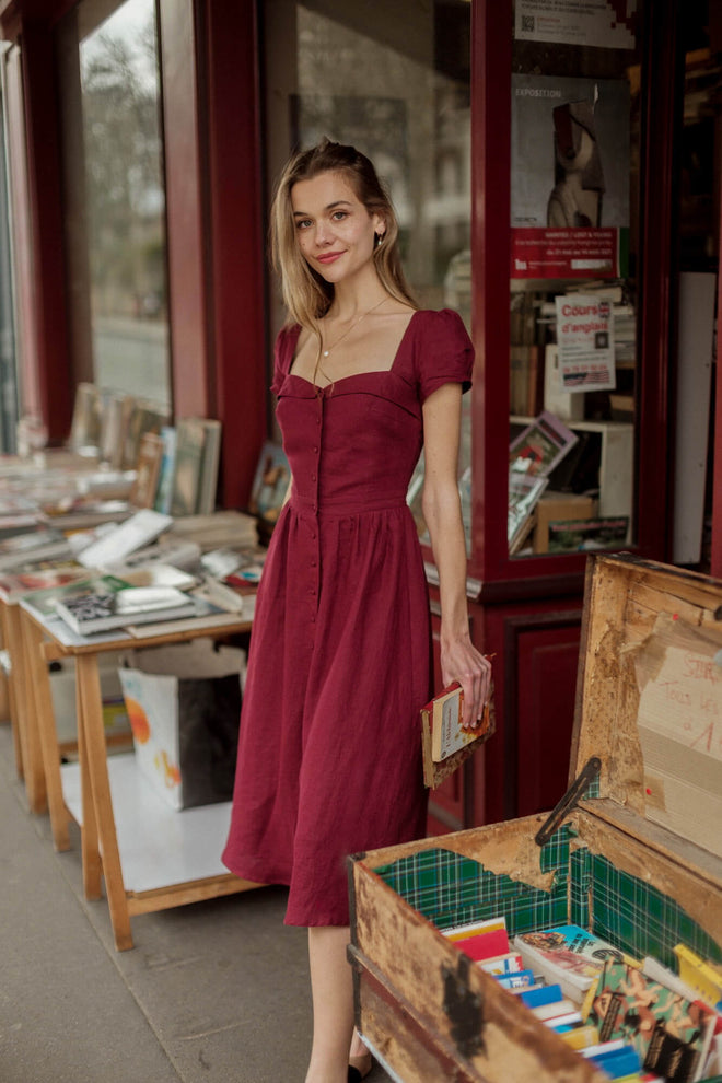 A long haired girl in Paris at a vintage book shop wearing a bordeaux button down Gaâla dress