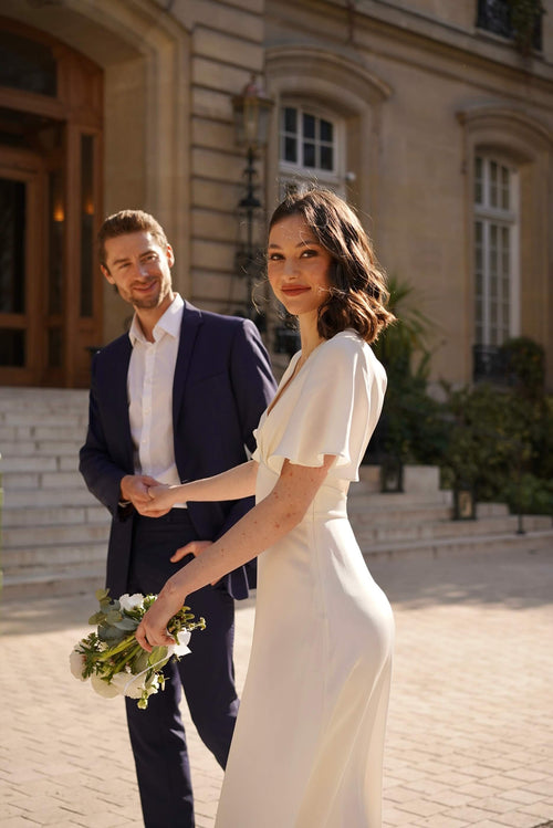 A happy bride in Paris wearing a long silk dress with flutter sleeves and an open back 