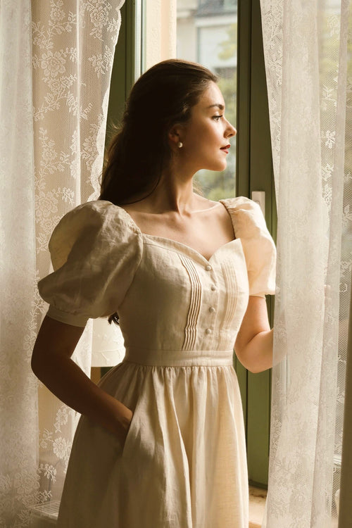 Shirin Altsohn in a vintage inspired cream linen dress leaning out of a window