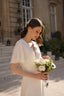 A happy bride on her wedding day in Paris wearing a silk dress with flutter sleeves and an open back