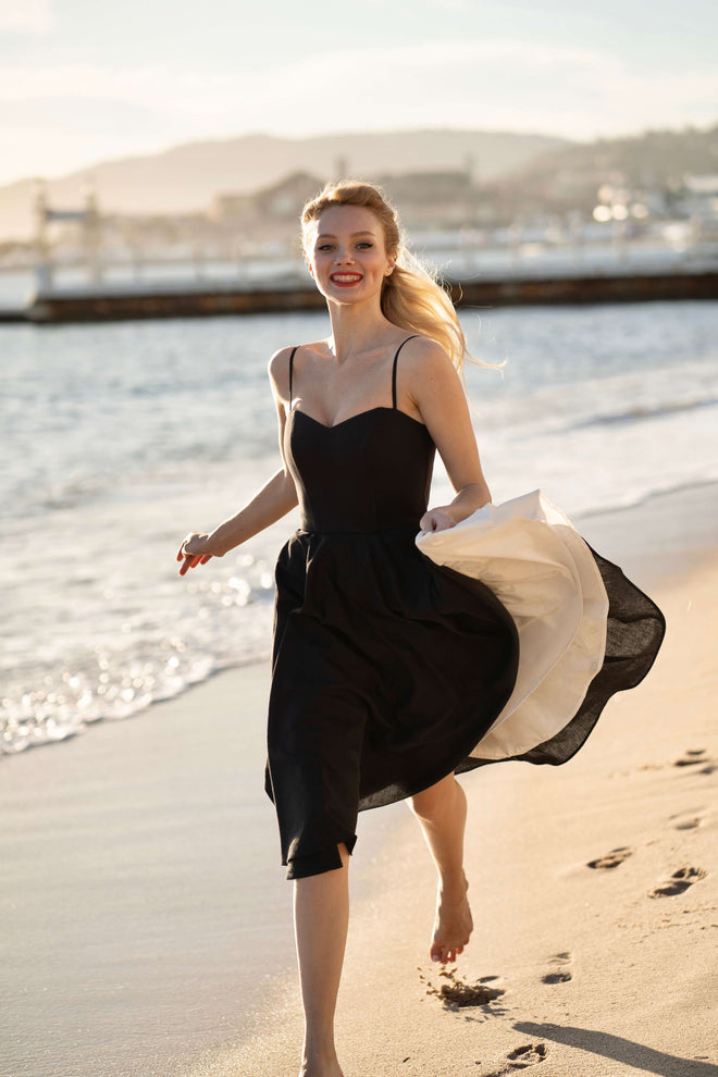 A girl recreating Brigitte Bardot’s iconic run on the beach in Cannes, wearing a Gaâla cotton/linen black Bardot dress.